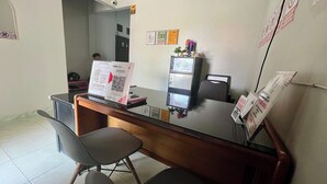 Een receptiebalie met een computer, een stoel en een klein tafeltje. Er hangen borden aan de muur en een kast met spullen erop.
