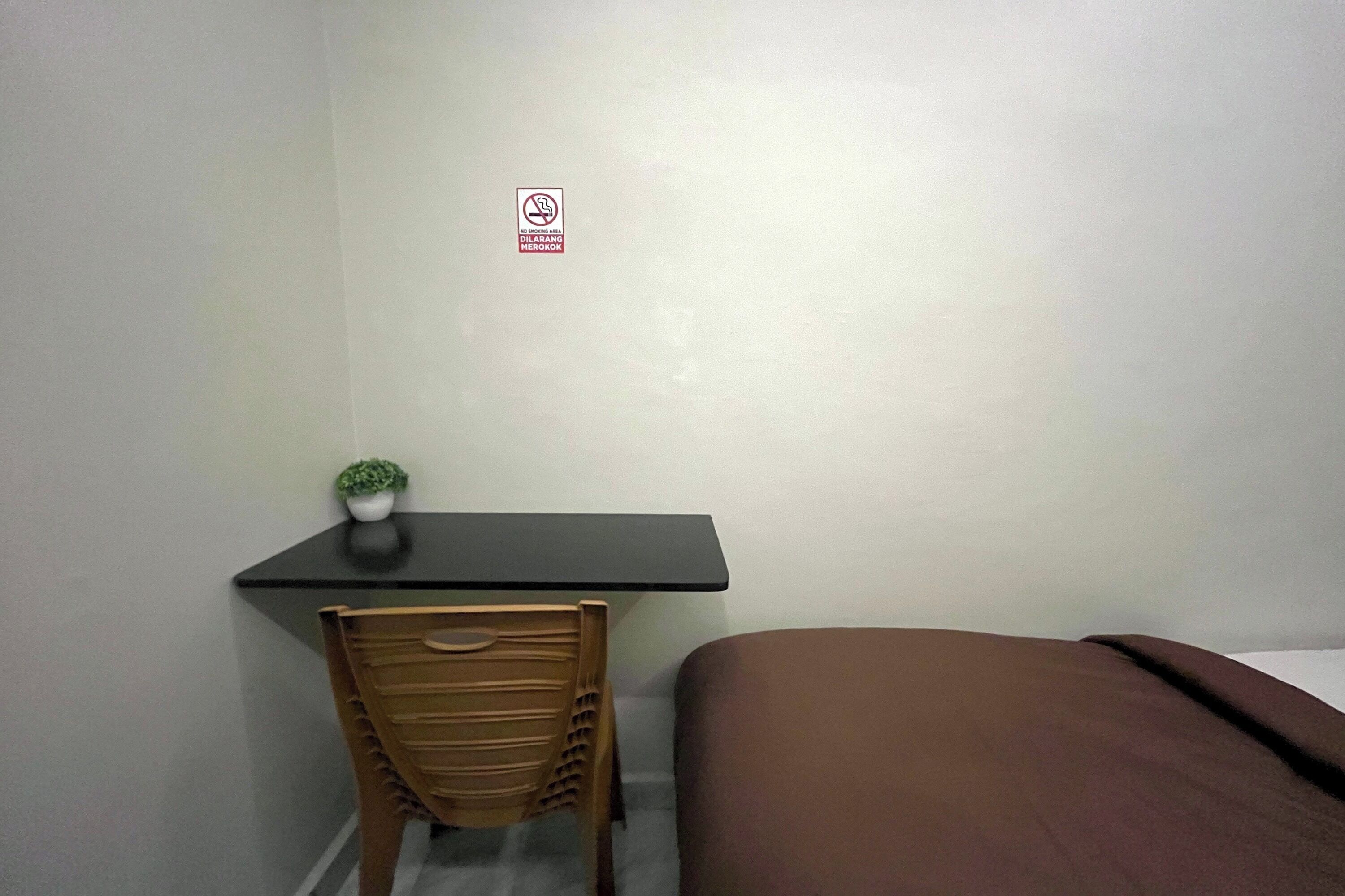 A small room with a desk, a chair, a bed, and a small potted plant.