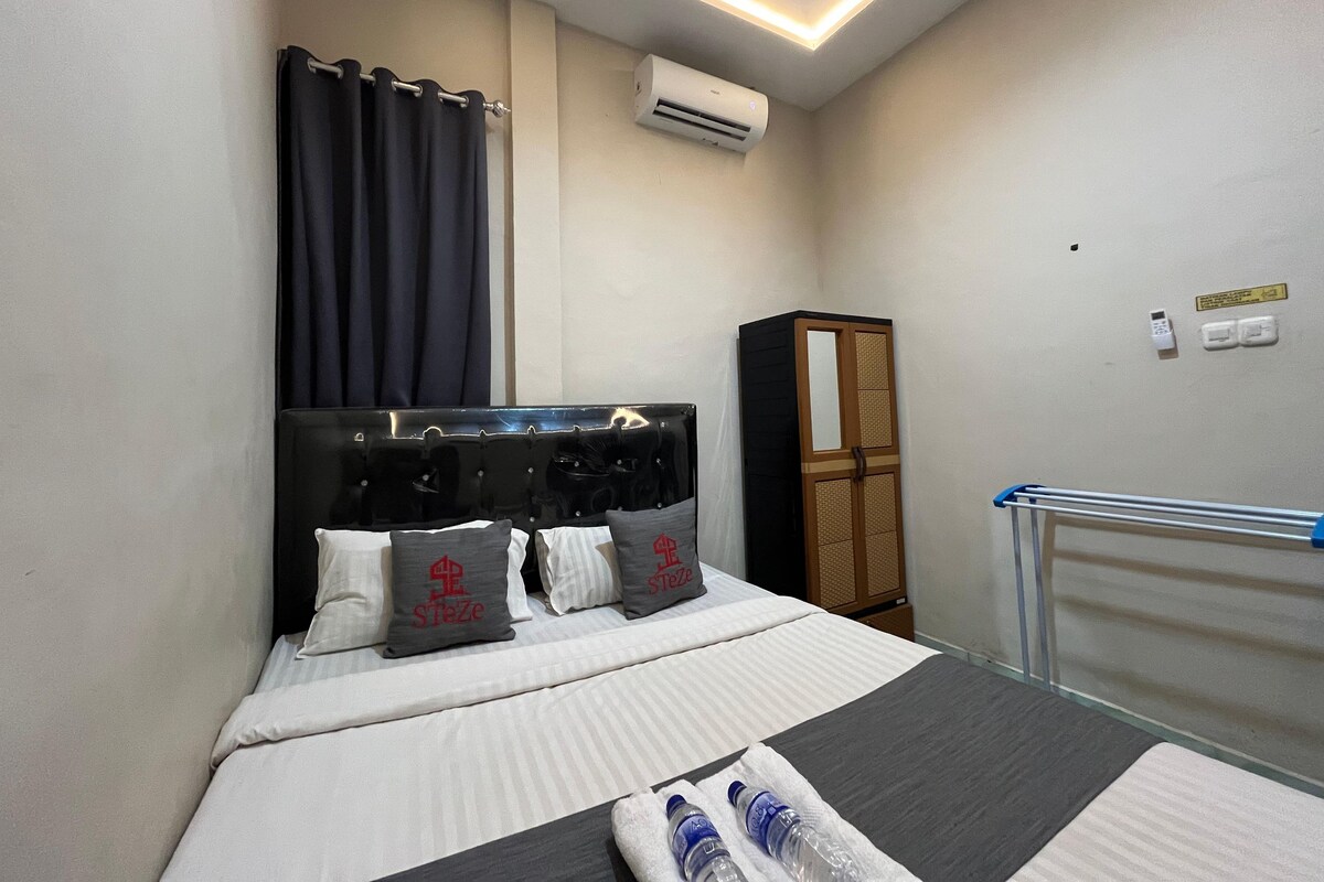 A neatly arranged hotel room with a bed, a wardrobe, an air conditioning unit, and a towel rack.
