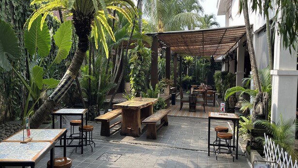 An outdoor café with wooden tables and benches, surrounded by lush tropical plants and palm trees. - R Residence Jakarta (Jakarta)