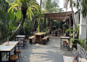 An outdoor café with wooden tables and benches, surrounded by lush tropical plants and palm trees. - R Residence Jakarta (Jakarta)
