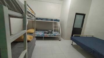 A dormitory room with bunk beds, a single bed, and a small window.