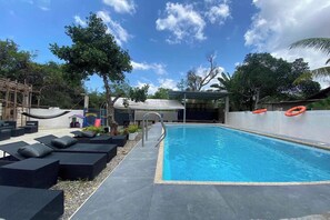 A swimming pool with lounge chairs and a covered area.