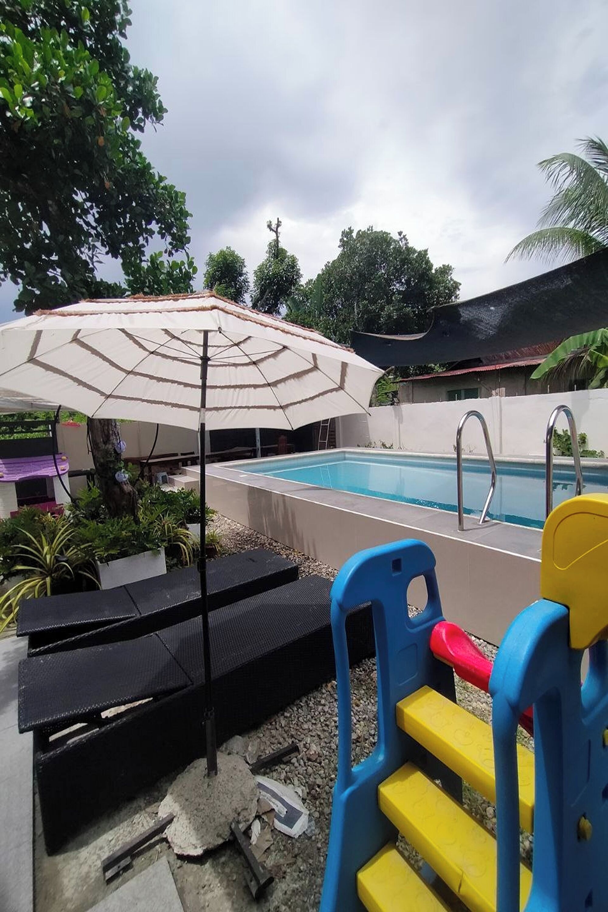 A swimming pool with a covered area, a children's play structure, and a bench.
