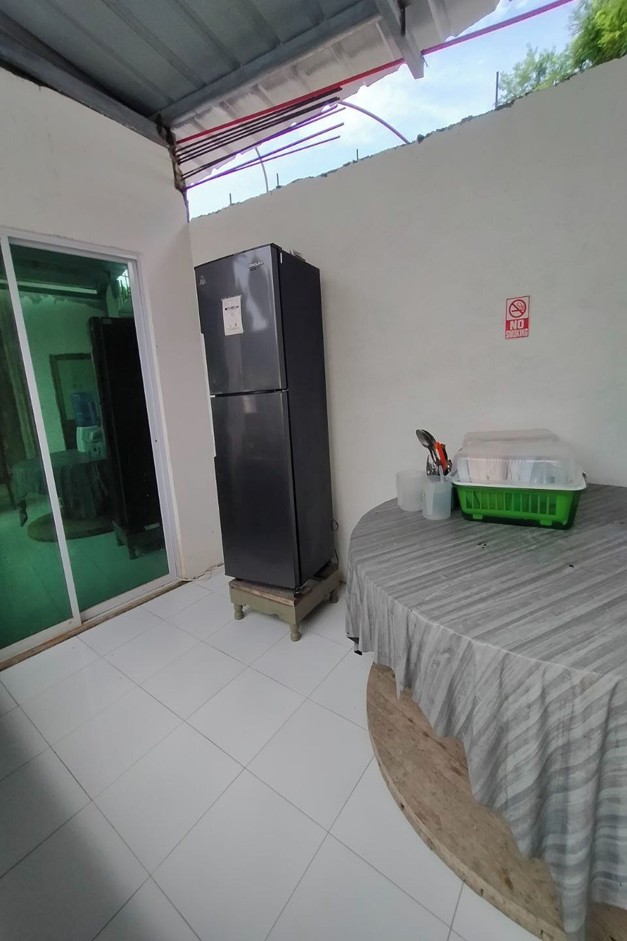 A room with a bed, a refrigerator, a trash bin, and a window.