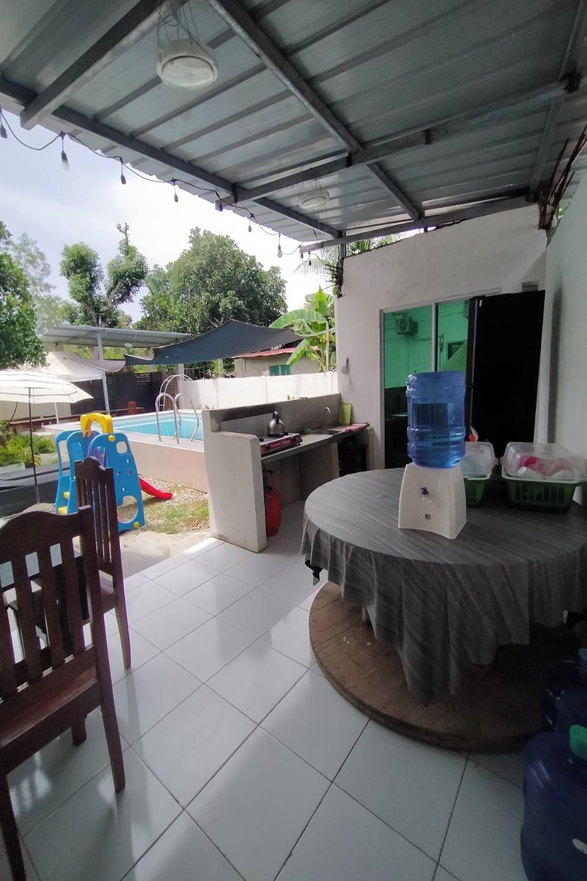 Un espace extérieur abrité comprenant une piscine, un distributeur d’eau et une table avec une chaise.