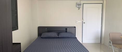 A bedroom with a bed, a chair, a door, and a wall-mounted electrical box.