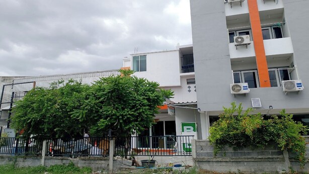 A multi-story building with air conditioning units, a green sign, and a metal fence. - Na Nont Place (Pak Kret)
