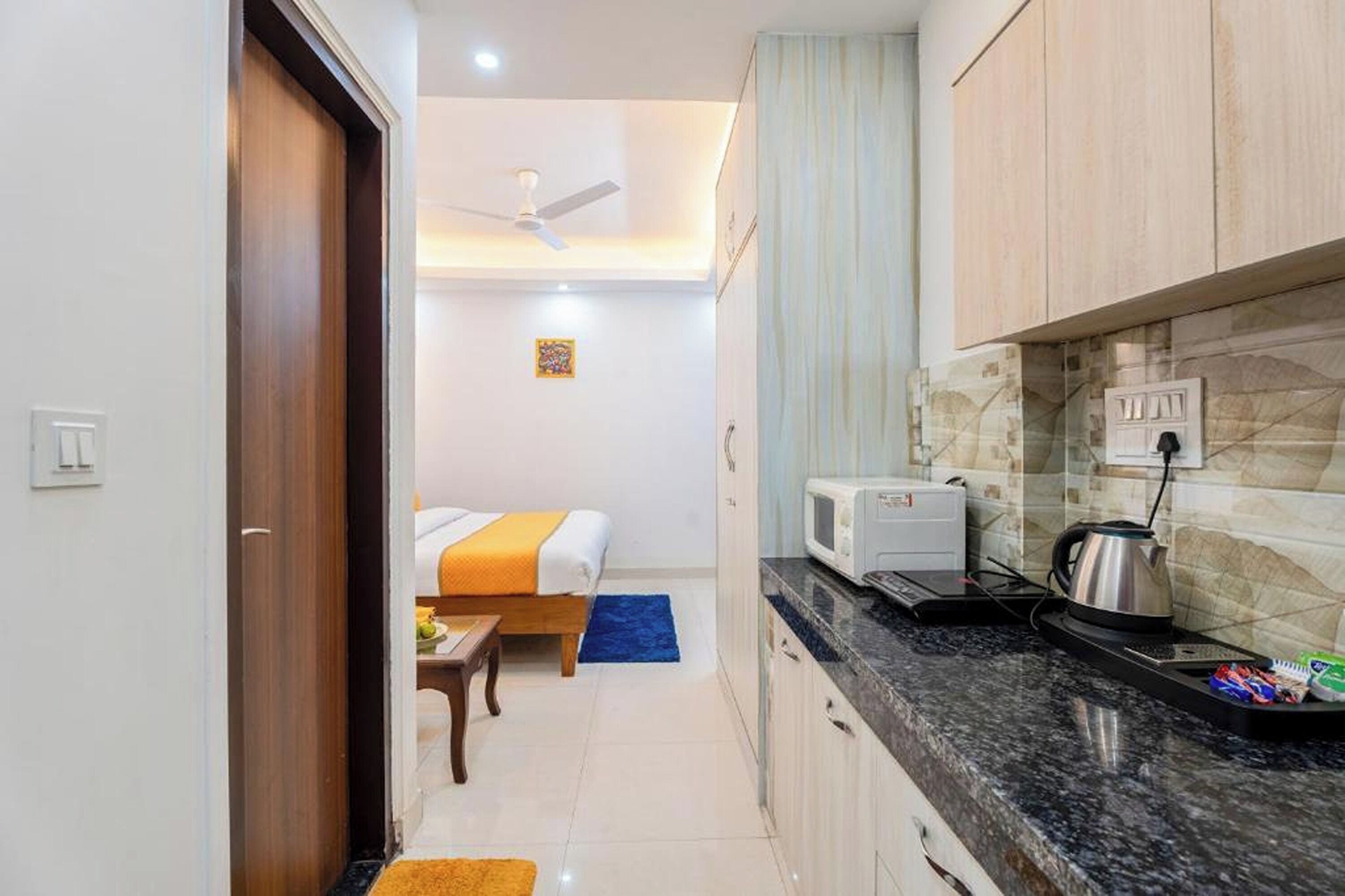 A compact hotel room with a bed, a small table, a microwave, and a kettle on the counter.
