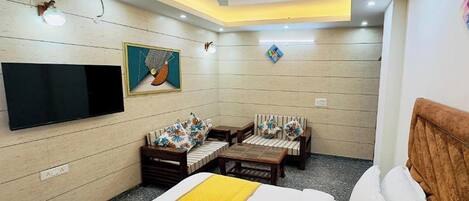 A hotel room with a bed, a sofa, a coffee table, a TV mounted on the wall, and a ceiling fan.