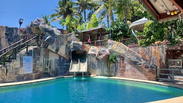 A pool with a waterfall feature, surrounded by tropical vegetation and a rocky wall.