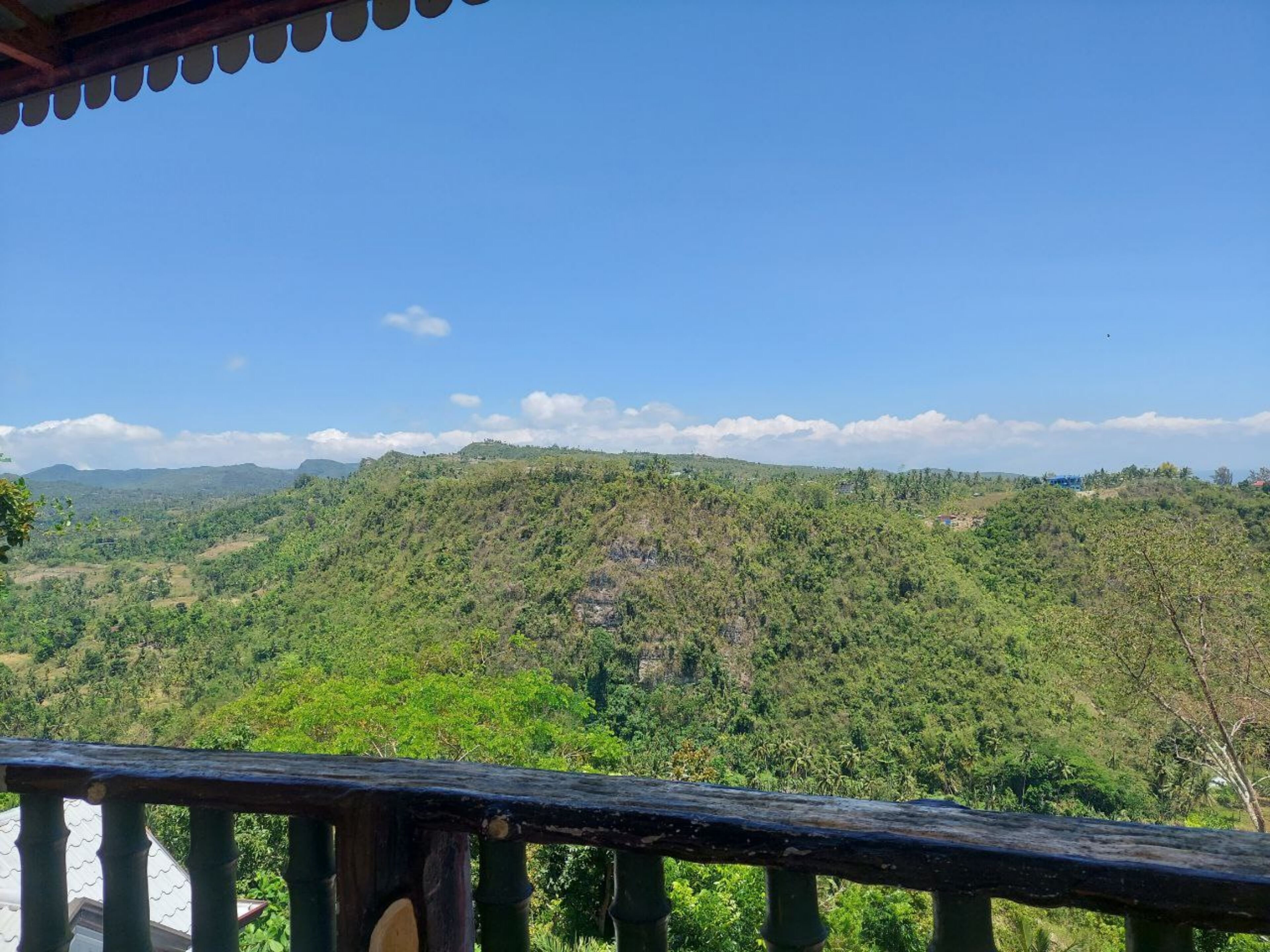 A view from a balcony overlooking a lush, green landscape with distant hills and a clear blue sky.