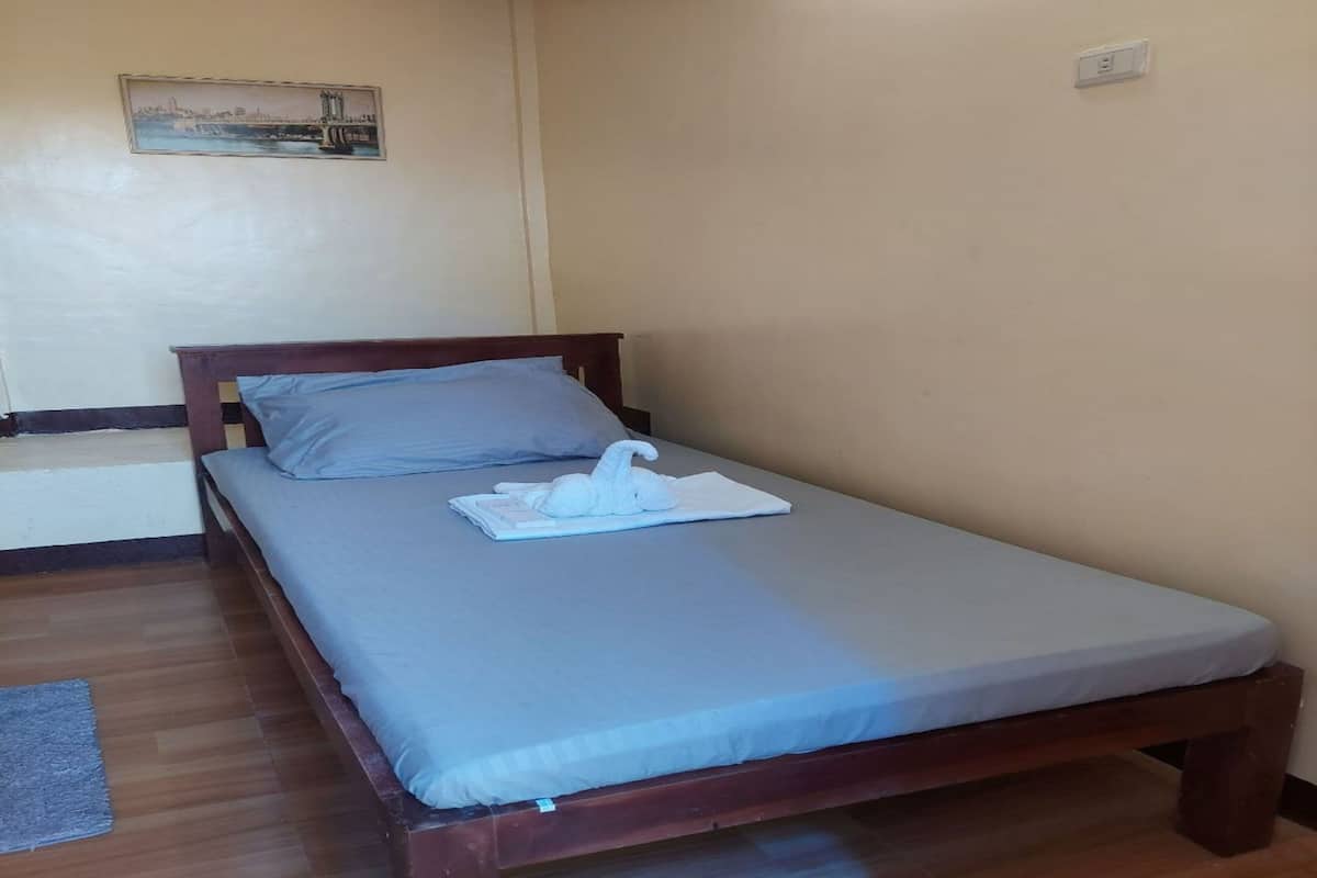 A single bed with a wooden frame and a grey mattress, a white towel, and a white pillow on the bed.