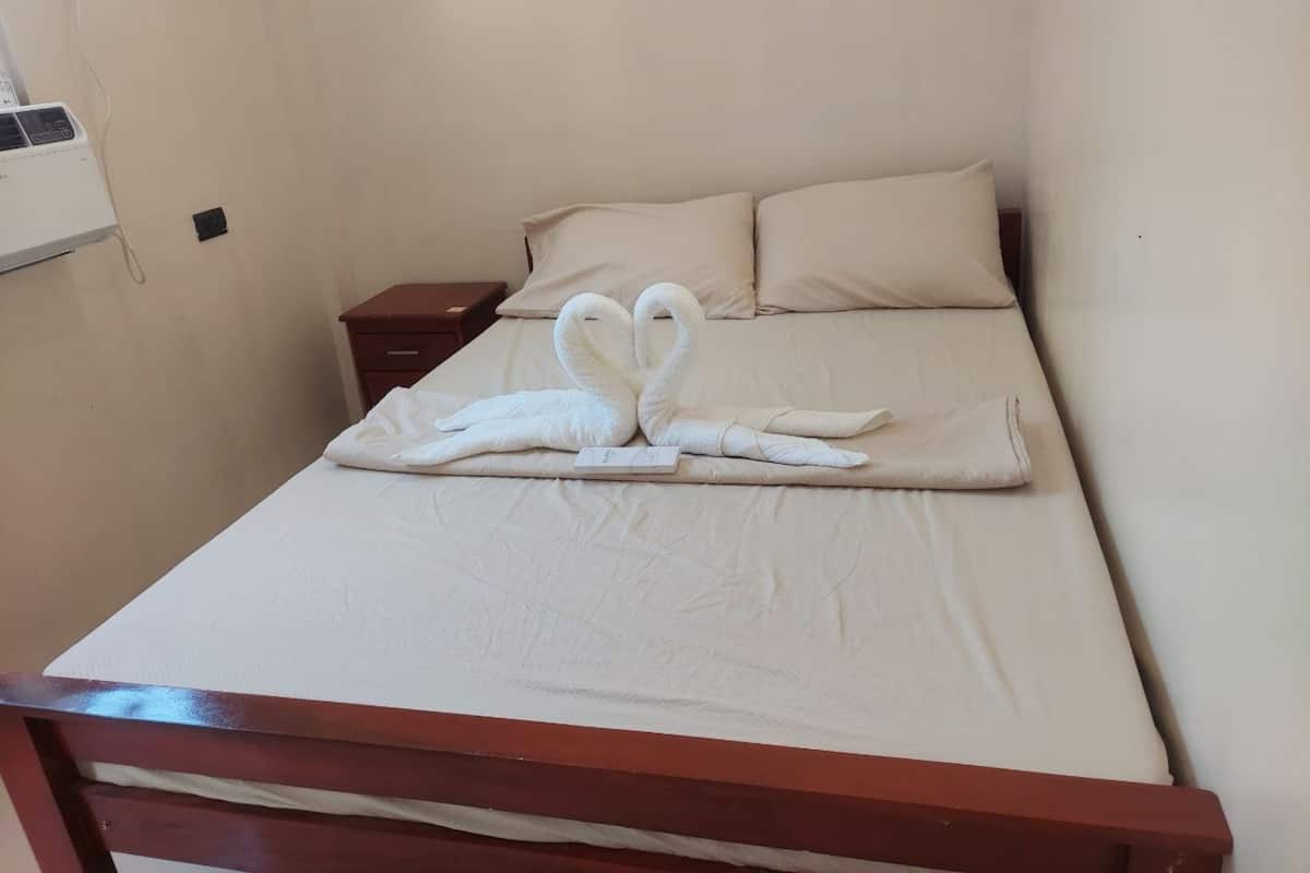 A neatly made bed with a towel swan decoration, a wooden headboard, and a small bedside table with a lamp.