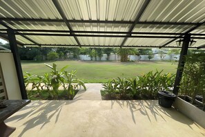 Un patio couvert avec un sol en béton, donnant sur une cour gazonnée.