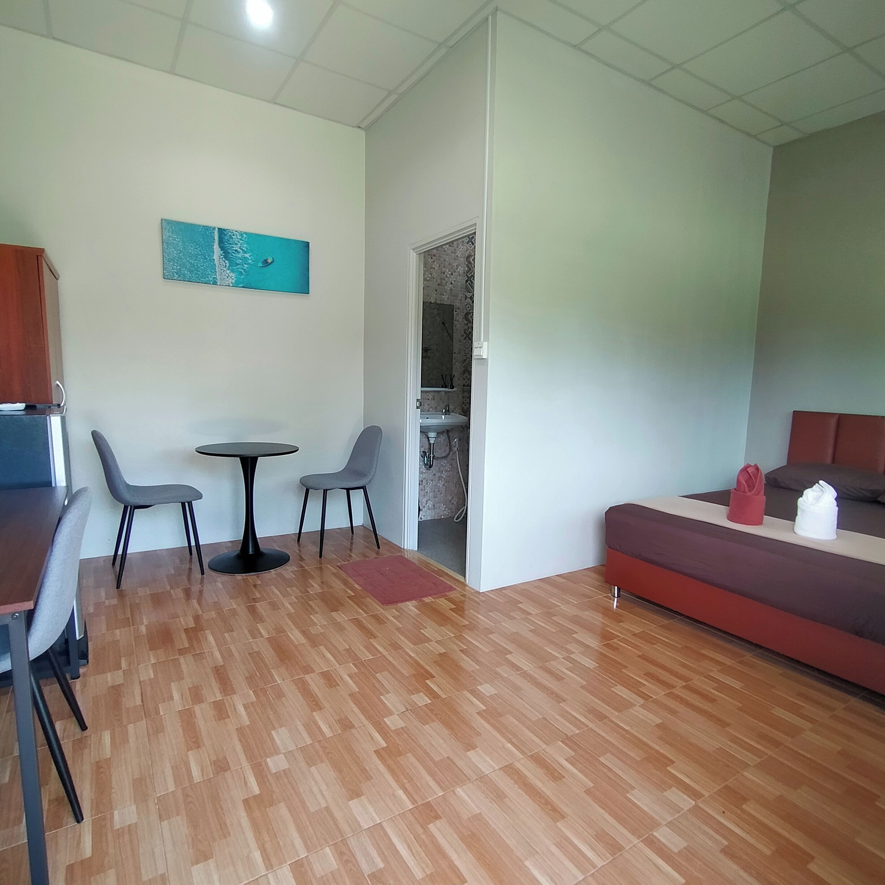 A modern living room with a wooden floor, a dining table with two chairs, a sofa, and a painting on the wall.