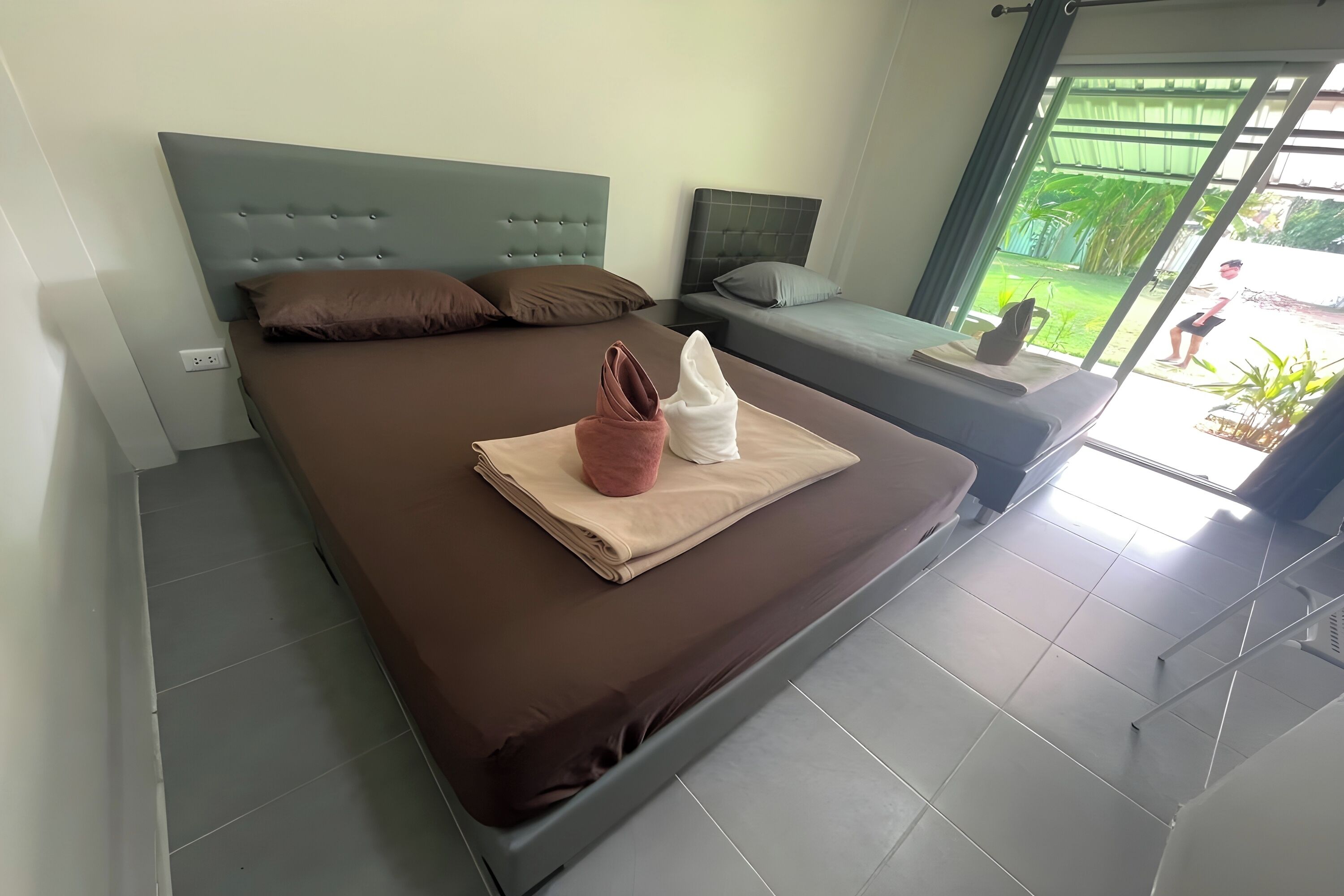 Ein Schlafzimmer mit einem großen Bett, einem kleinen Sofa und einem Fenster mit Blick auf Grünflächen.