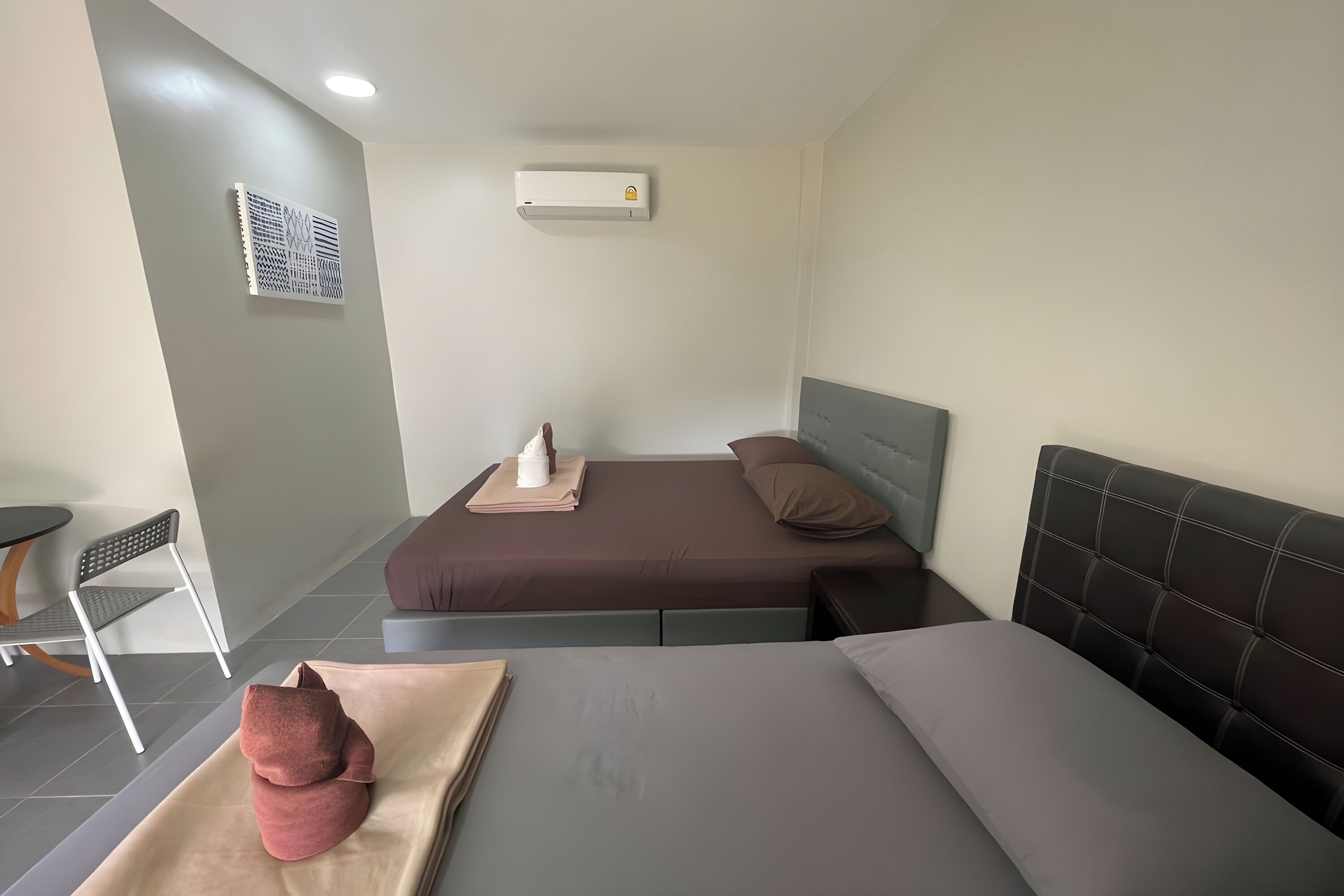 A hotel room with two beds, a small table, a chair, and an air conditioning unit.