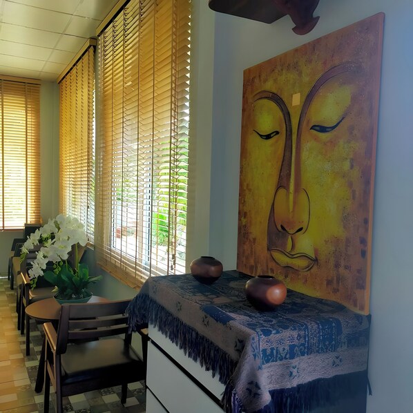 A dining area with wooden blinds, a table with a blue fringed tablecloth, two ceramic vases, and a large abstract painting on the wall. - Davy'S Cottage Phuket (Thep Krasattri)