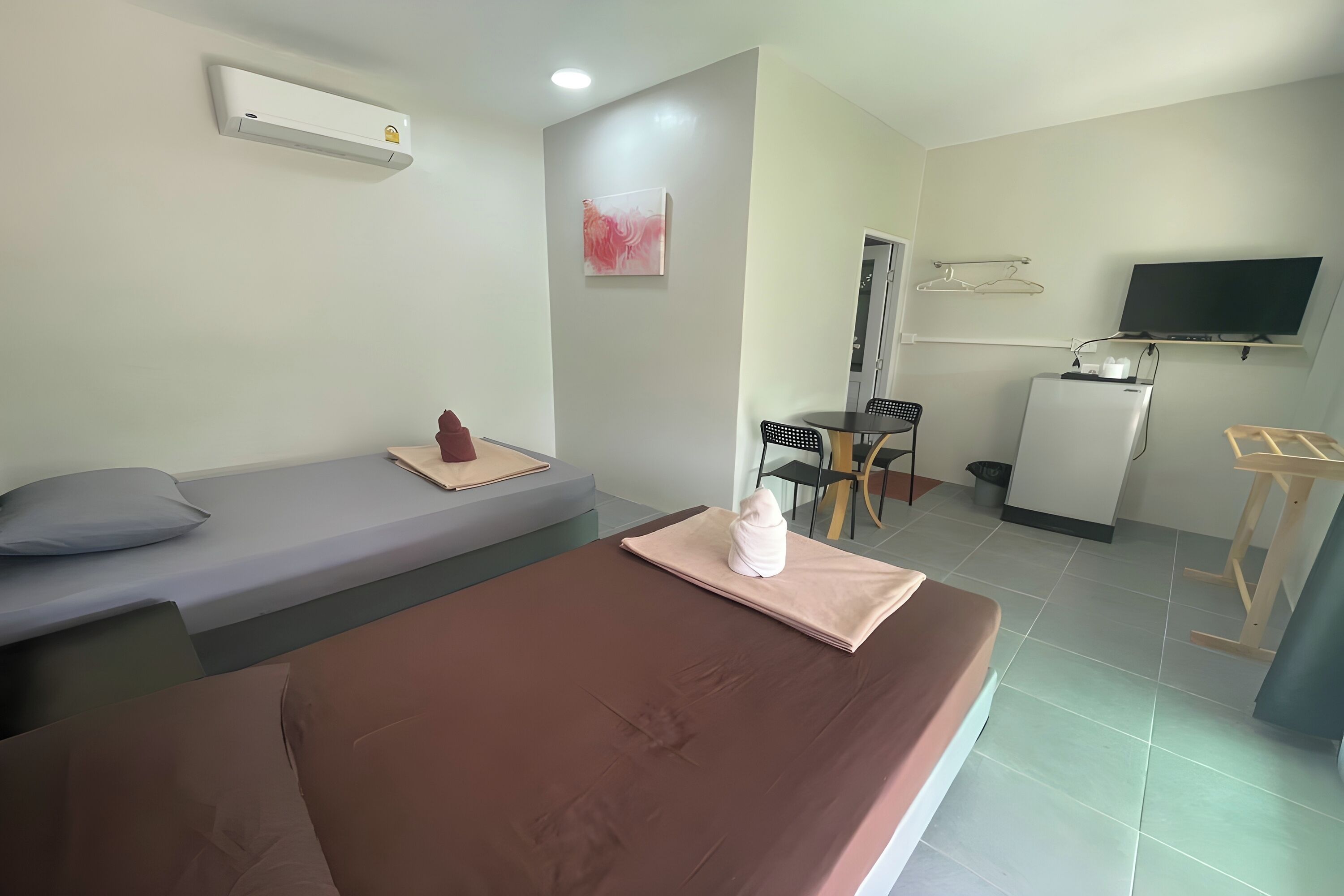 A hotel room with a bed, a small desk, a chair, a TV, and a wall-mounted air conditioner.