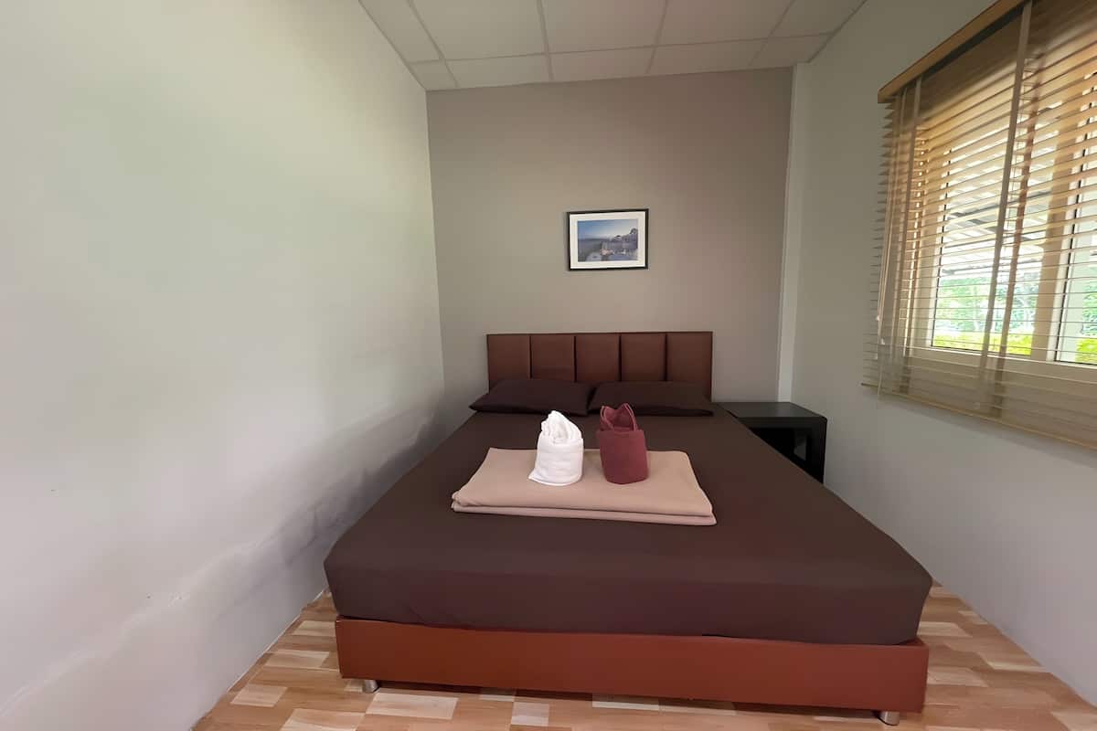 A neatly made bed with a brown mattress, a white towel, and a red bag on top.
