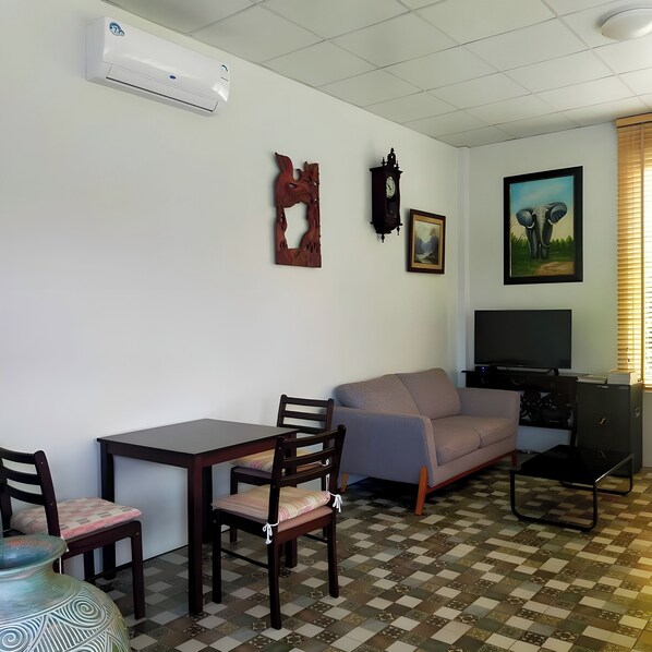 Un salon avec un canapé, un téléviseur, une horloge et un tableau encadré accroché au mur.