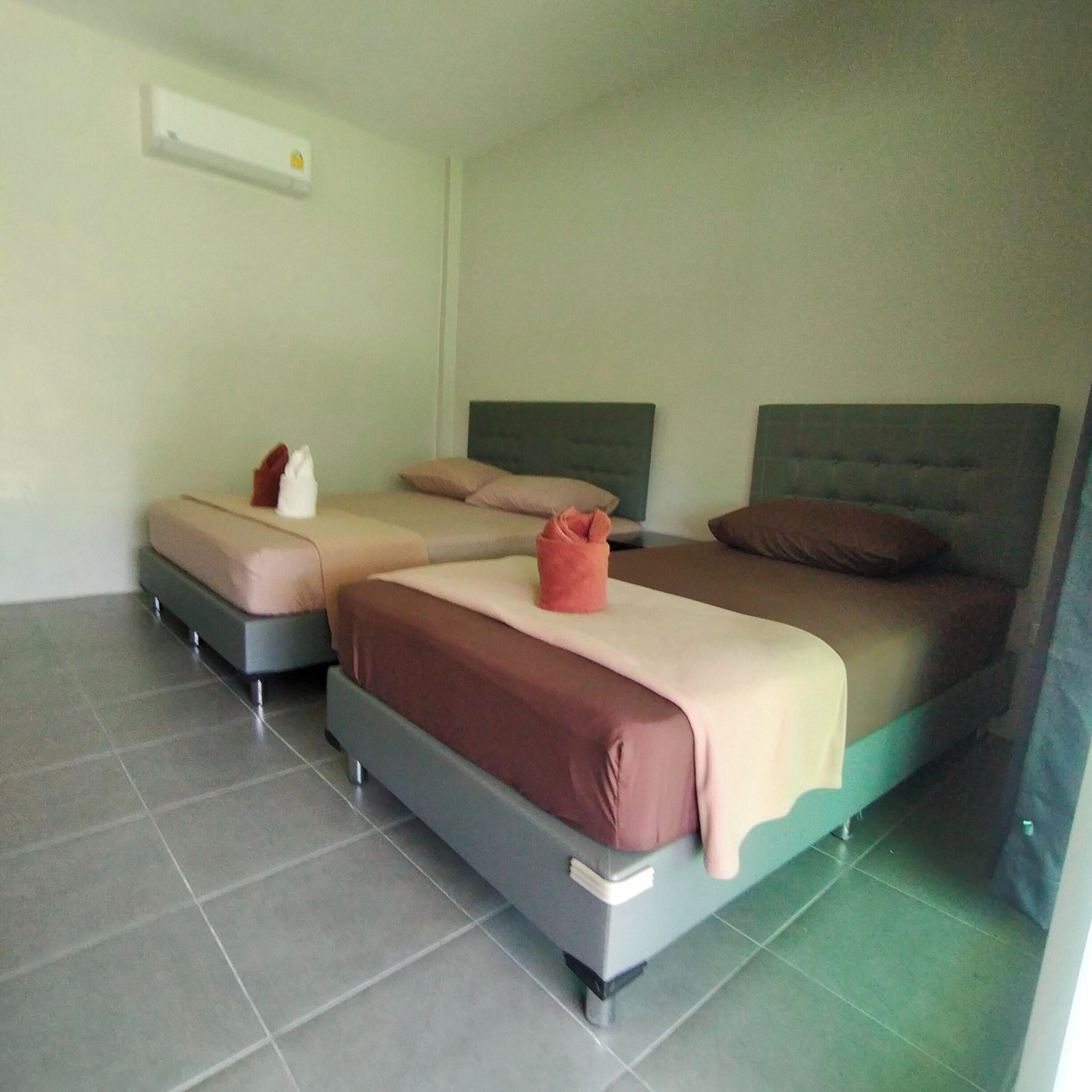 A hotel room with two beds, a small table, and a wall-mounted air conditioning unit.