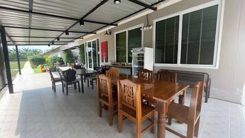Alpendre coberto com mesa e cadeiras de jantar, janelas amplas e área de cozinha.