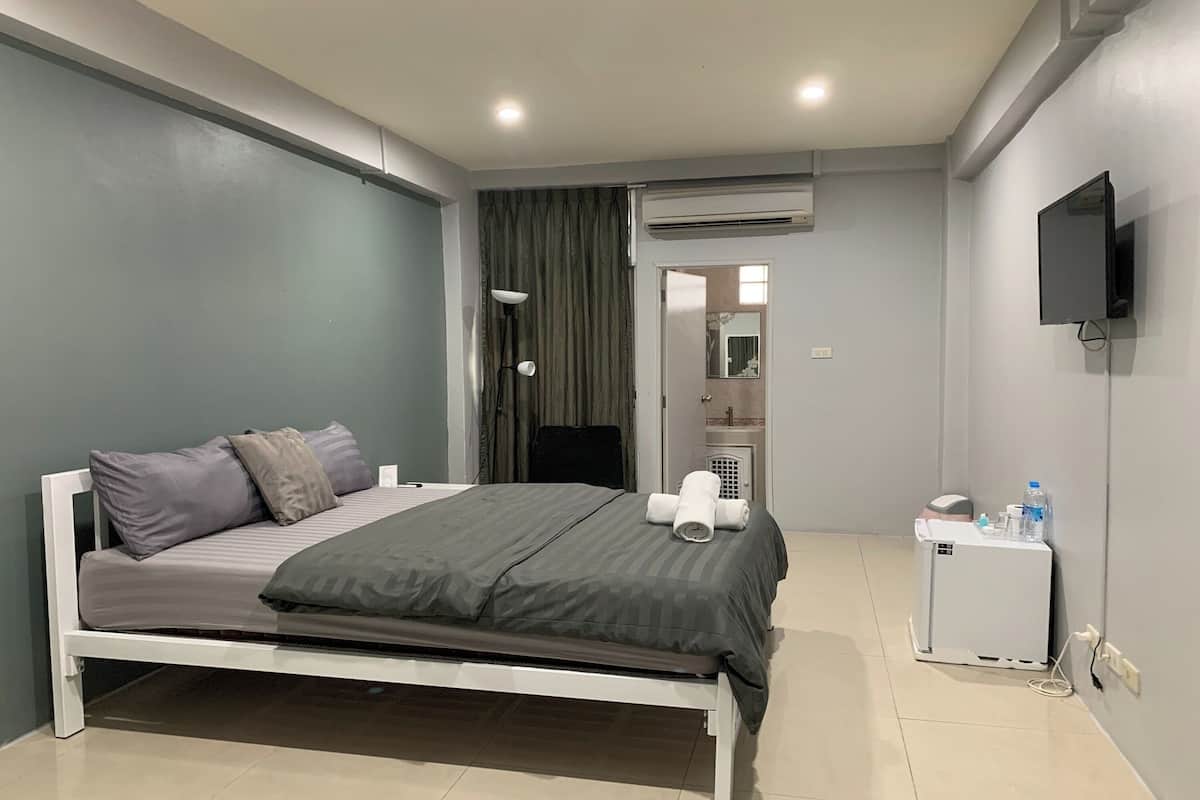 A modern hotel room with a bed, a small bedside table with a lamp, an air conditioning unit, a television, and a water dispenser.