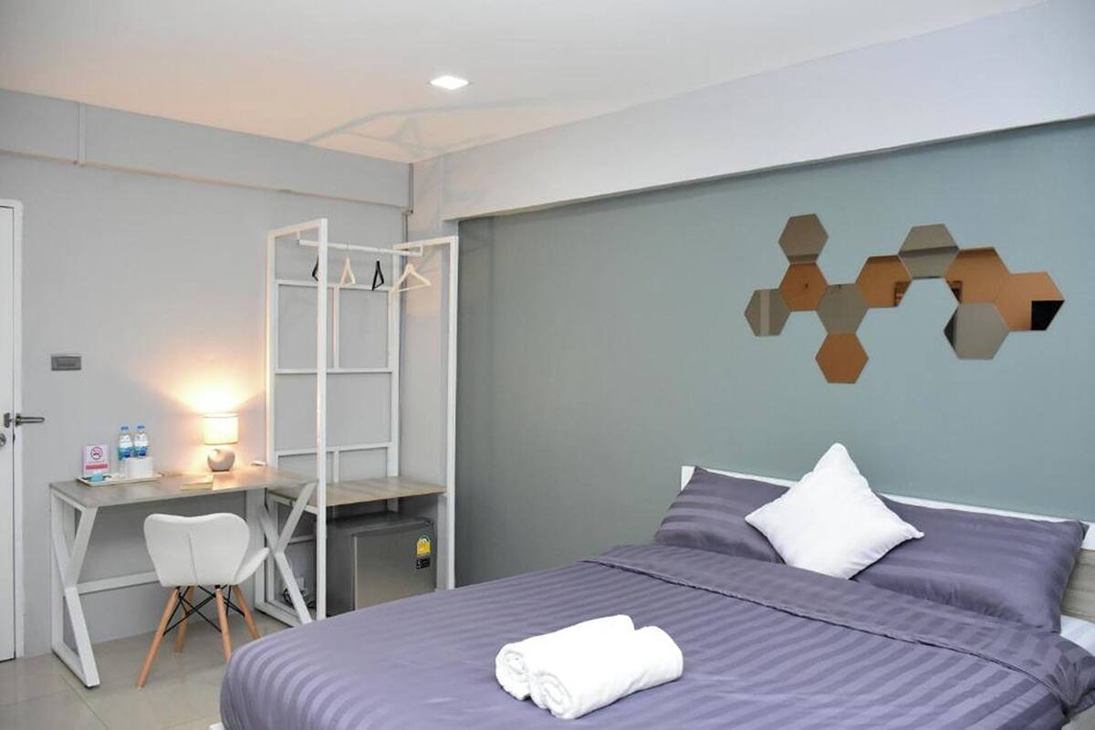 A hotel room with a bed, a desk, and a chair. There is a wall art piece above the bed.