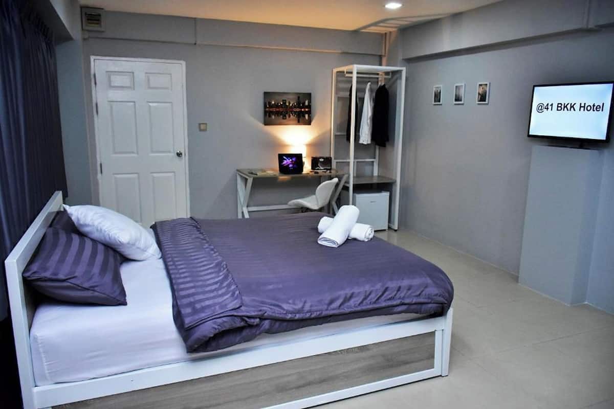A modern hotel room with a bed, a desk with a computer, a TV, and a wardrobe.