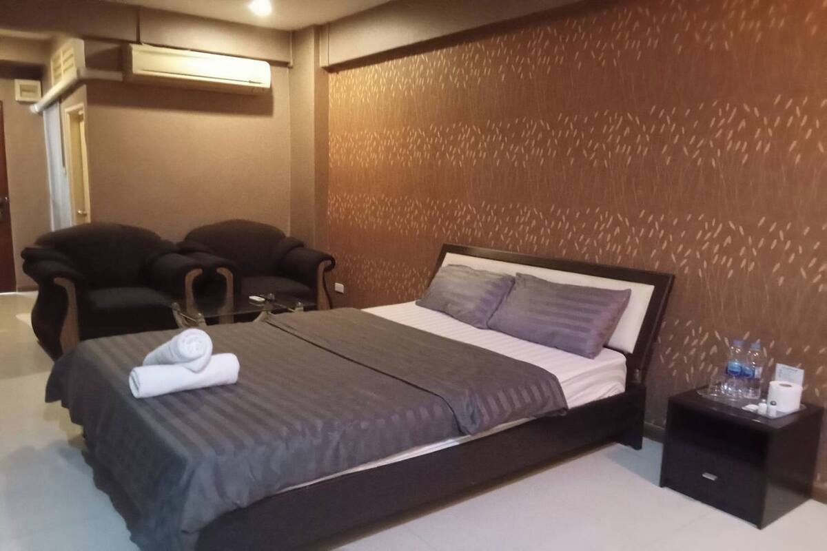 A hotel room with a large bed, two armchairs, a small table with toiletries, and a patterned wall.