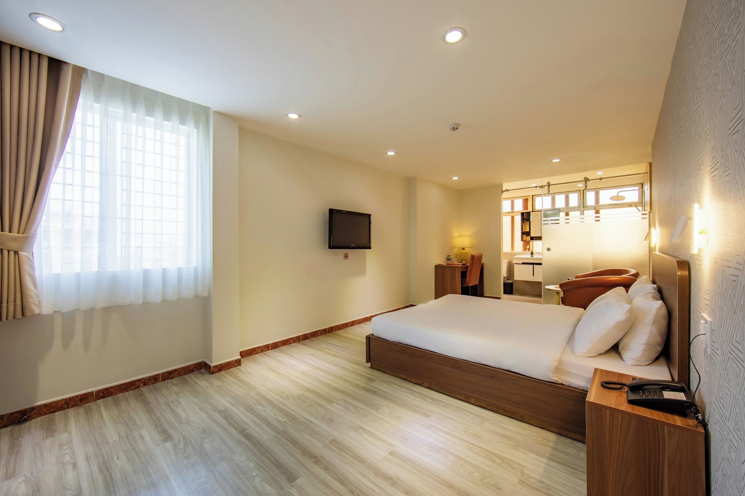 A modern hotel room with a large bed, a bedside table, a TV mounted on the wall, and a bathroom with a mirror and lights.