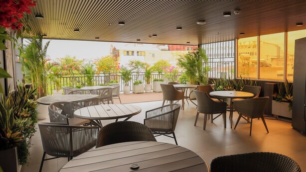 An outdoor patio area with round tables and wicker chairs, surrounded by potted plants and overlooking a cityscape. - Lanura Saigon Boutique Hotel (Ho Chi Minh City)