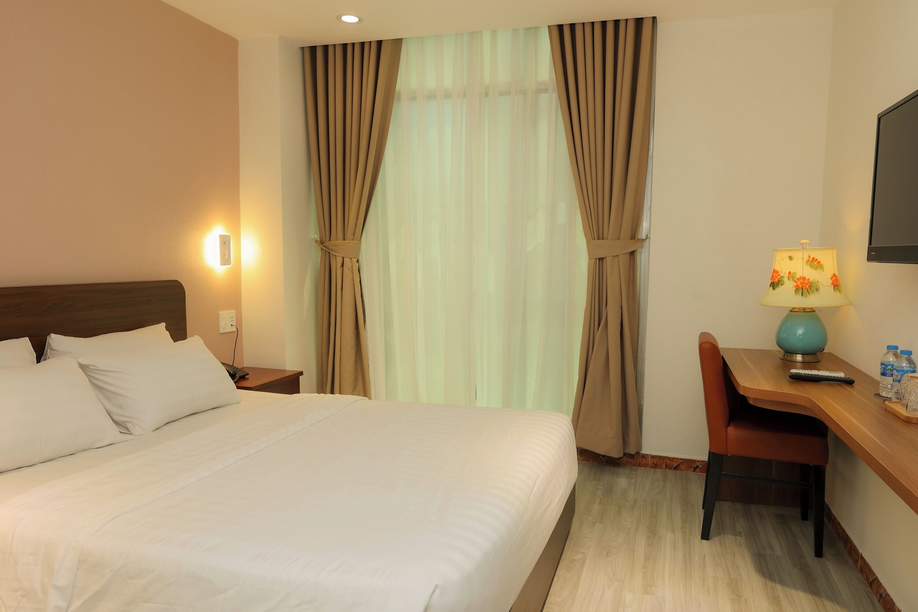 A hotel room with a large bed, a desk with a lamp, and curtains.