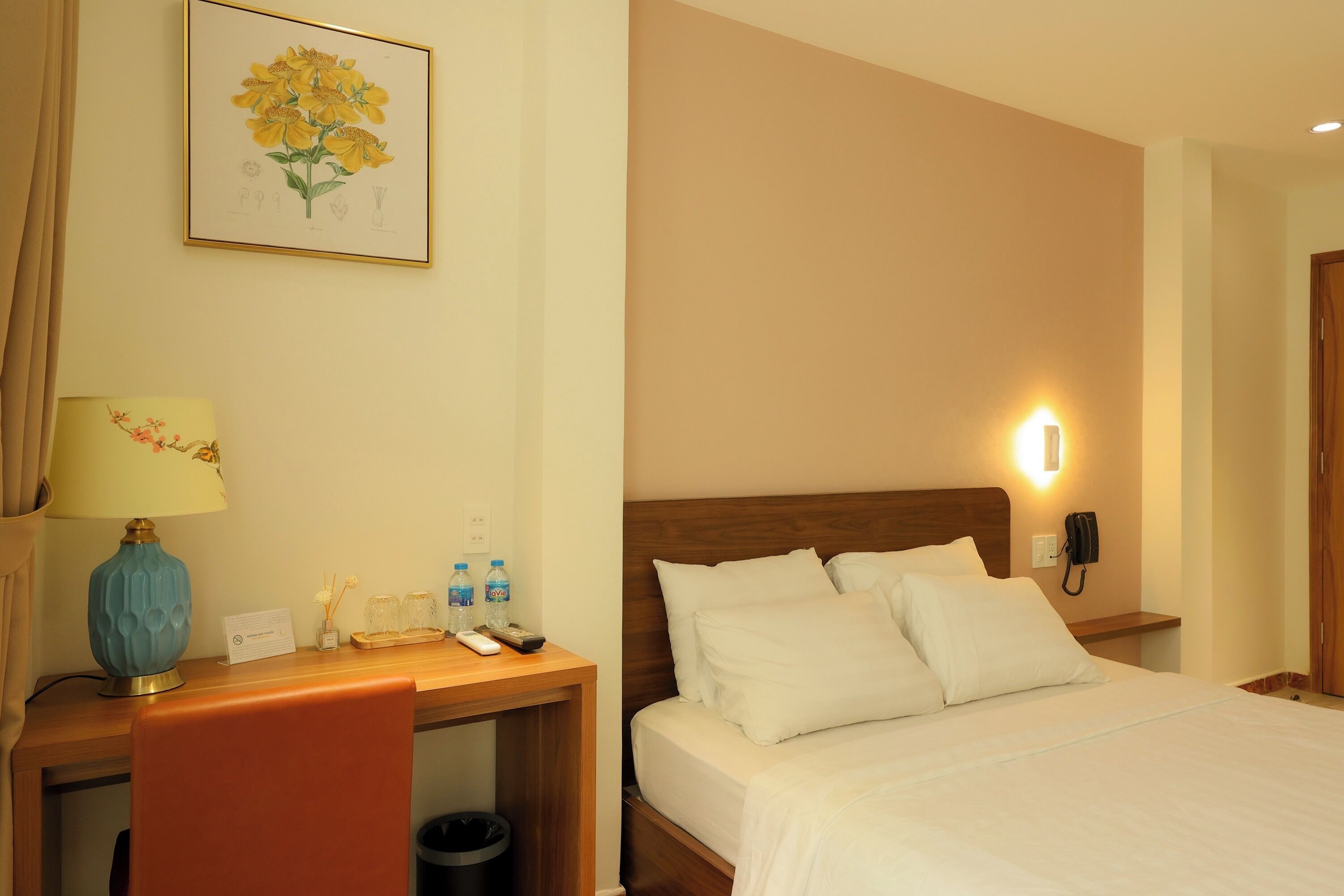 Una camera d'albergo con un letto, un comodino, una lampada e una stampa botanica incorniciata appesa al muro.