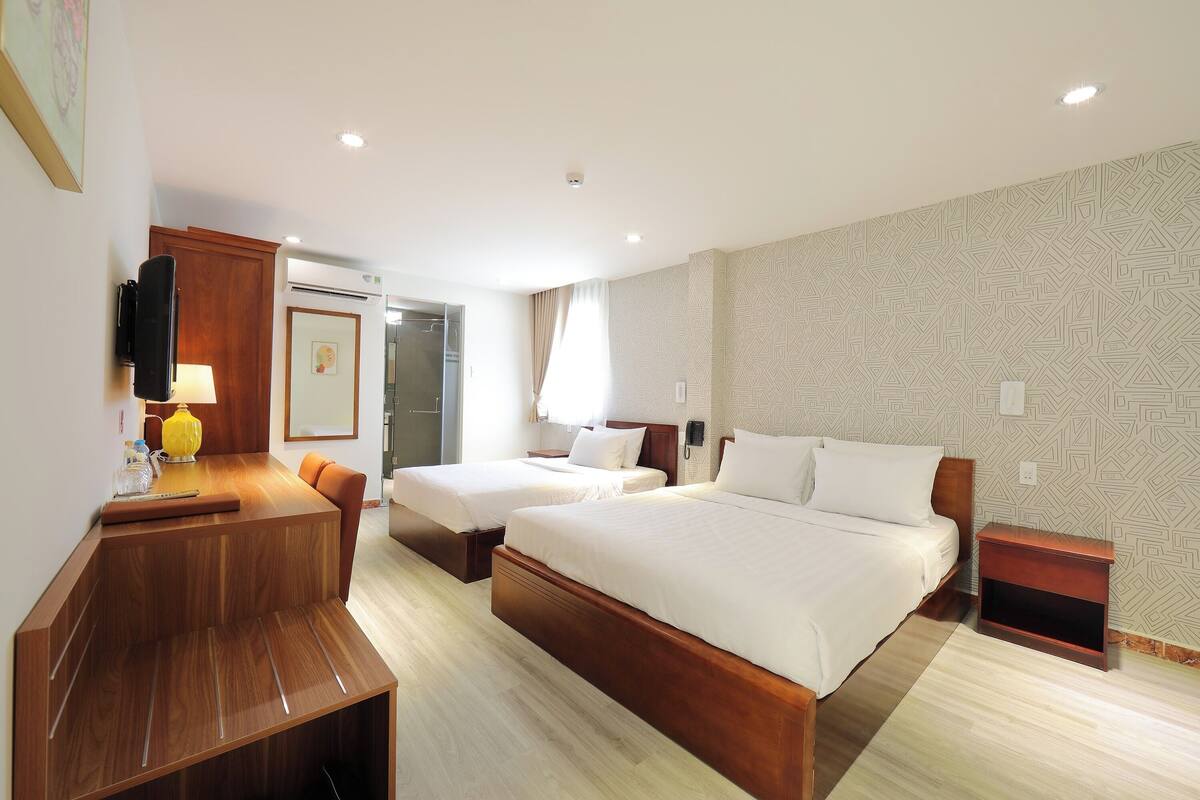Une chambre d’hôtel avec deux lits, un bureau, une chaise, une lampe et une petite table.