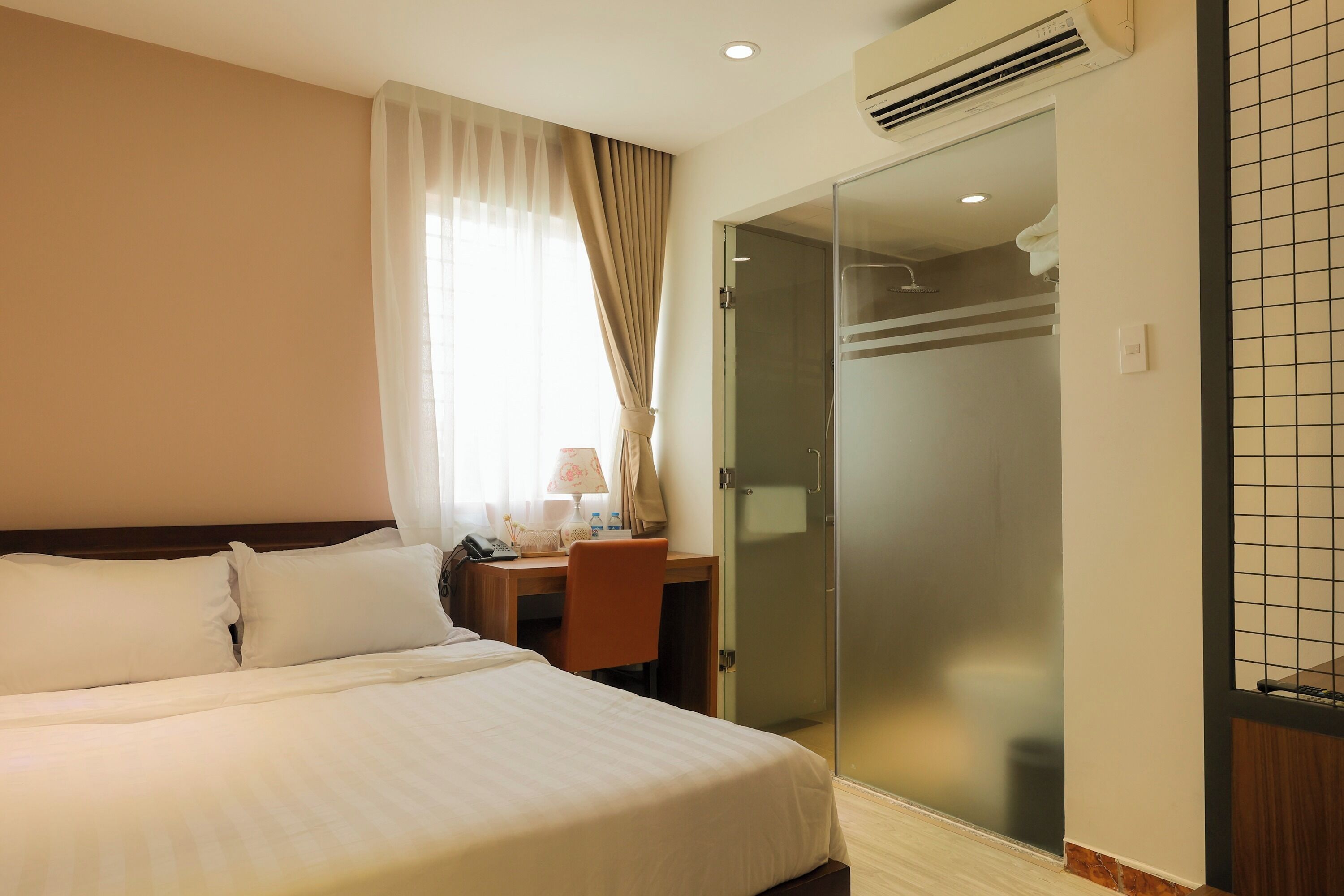 A hotel room with a bed, a desk with a chair, a shower area, and a glass door.