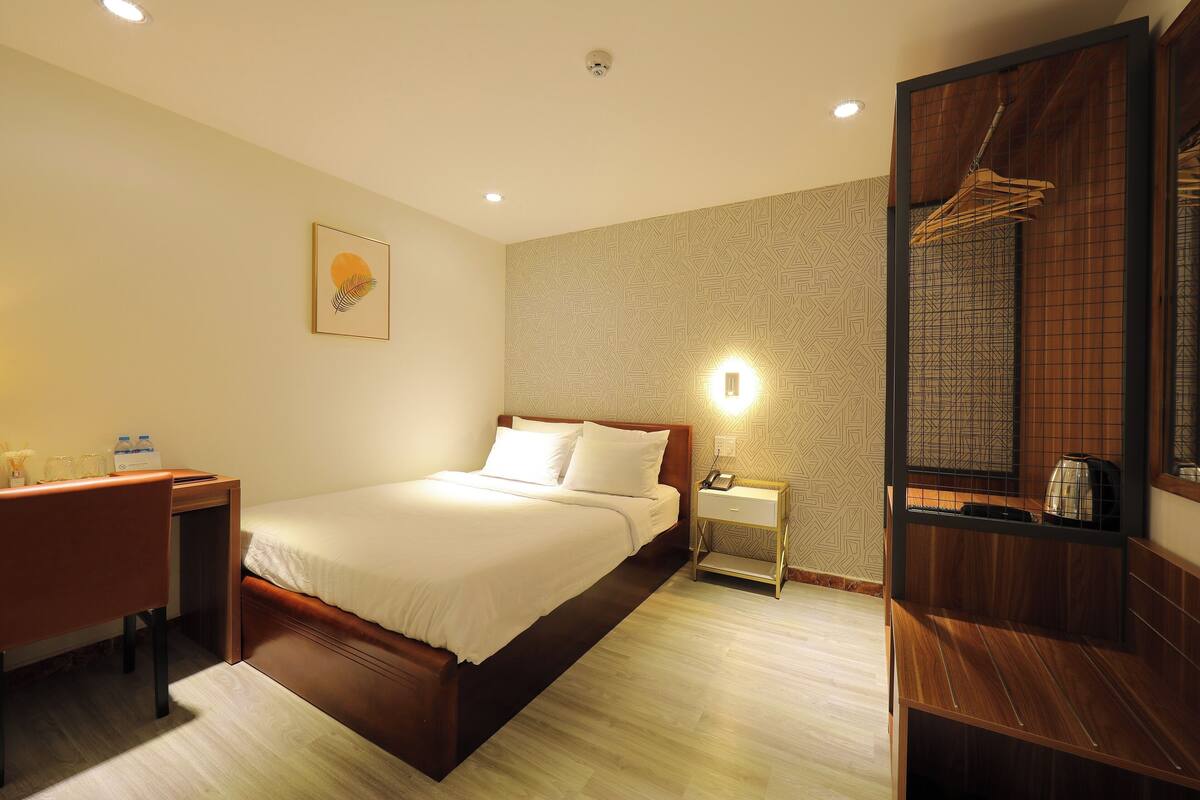 Une chambre d’hôtel avec un lit, une table de chevet et un miroir doté d’un cadre en bois.