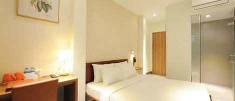 A hotel room with a bed, desk, chair, lamp, and a framed botanical illustration on the wall.