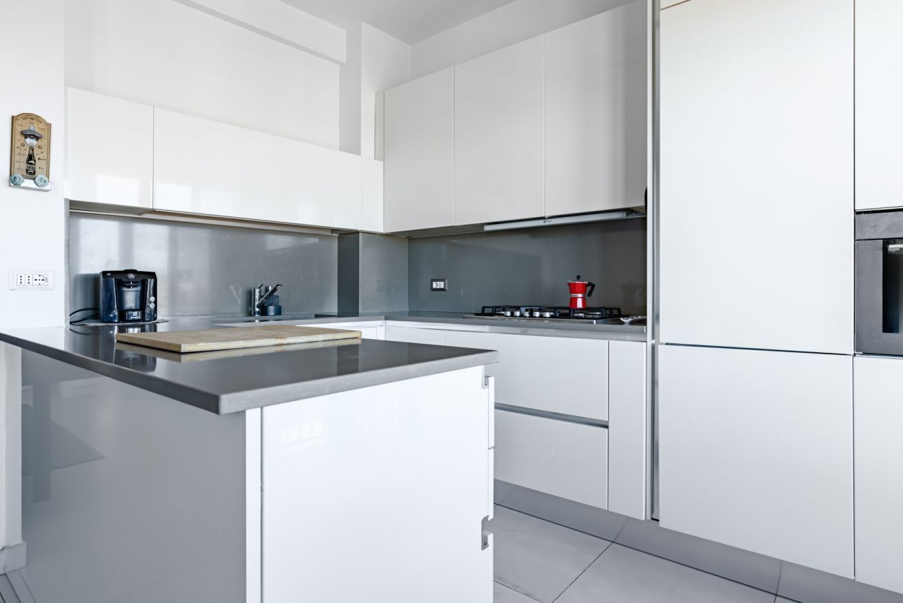 Una cucina moderna con mobili bianchi, un piano di lavoro in acciaio inossidabile e un fornello a gas.