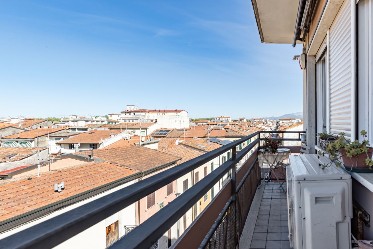 A balcony with a view of a cityscape, including buildings with red-tiled roofs and a clear sky.