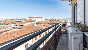 A balcony with a view of a cityscape, including buildings with red-tiled roofs and a clear sky.