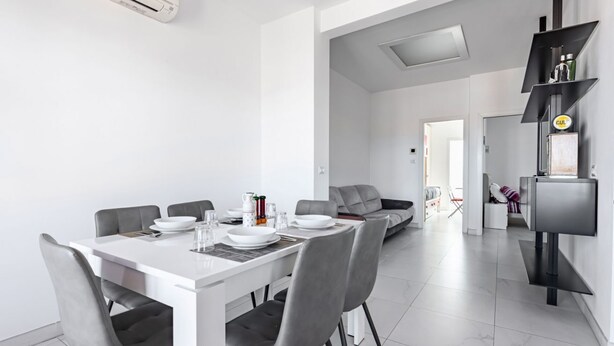 A modern dining area with a white table, grey chairs, and a built-in air conditioning unit.