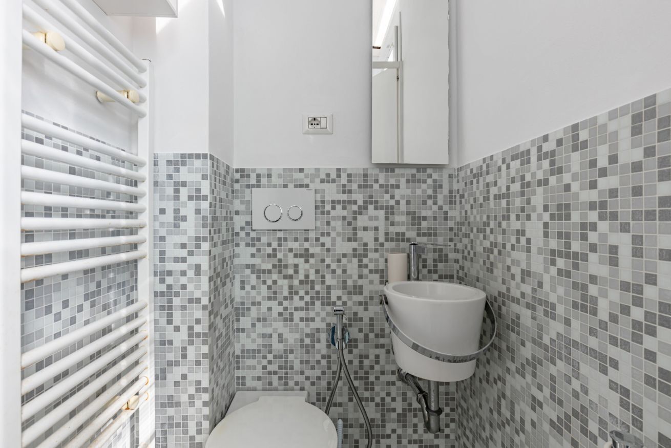 A bathroom with a toilet, a sink, a mirror, and a tiled wall.