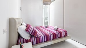 A modern bedroom with a bed, a hanging light fixture, and a window.