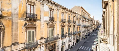 A row of historic buildings with balconies, a clear street, and parked cars.