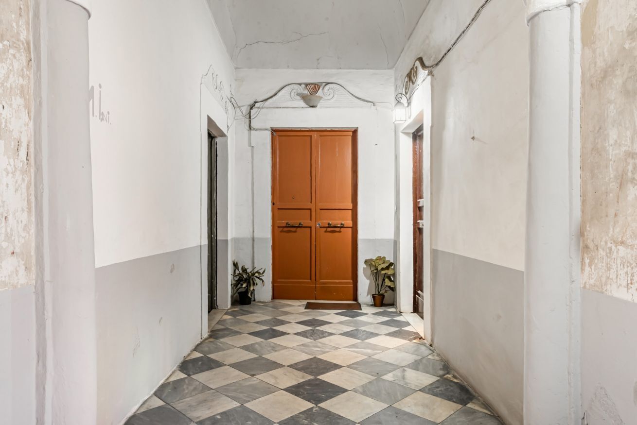 Un corridoio con pavimento a scacchi, una porta in legno e piante in vaso.