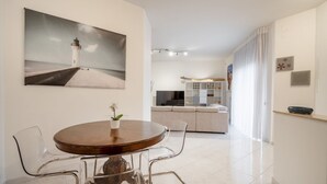 Un coin repas avec une table ronde, des chaises transparentes, une plante en pot et un tableau représentant un phare.