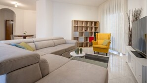 Un salon moderne avec un canapé d’angle, un fauteuil jaune, une table basse et une bibliothèque intégrée.